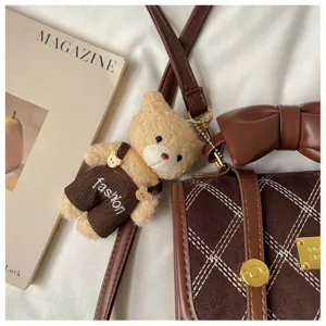 Brown shoulder bag detail featuring a cute teddy bear plush pendant and chic bow design.