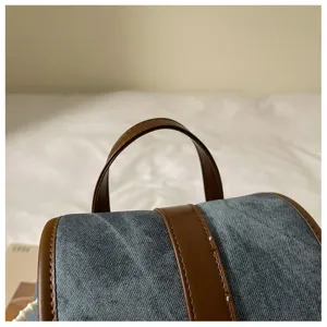 Close-up detail of the stylish denim backpack with brown leather handle and trim, clear view.