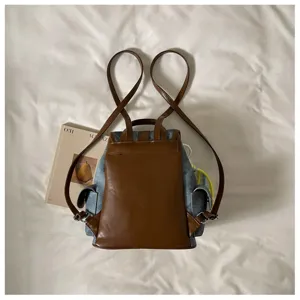 Stylish denim and brown leather backpack, casual daily commuter school bag with roomy storage.