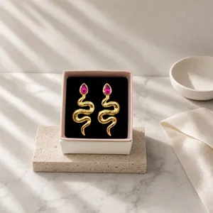 Closeup of retro gold snake earrings with pink gemstone in a box on marble surface.