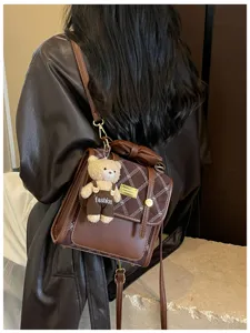 Detail view of brown leather backpack featuring a cute teddy bear pendant and plaid flap.