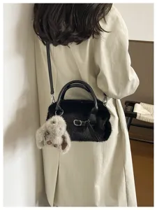 Close-up of black fluffy plush handbag with cute bunny charm, stylish shoulder strap detail.