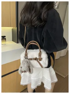 Detail shot of fluffy plush crossbody bag in white with brown straps and cute bunny charm.
