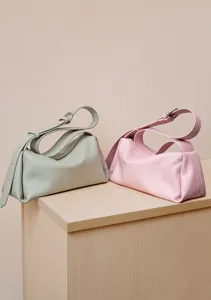 Vista detallada de elegantes bolsos de cuero verde pastel y rosa sobre soporte de madera.