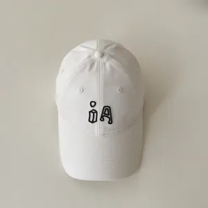 Children baseball cap detail shot, soft white cotton fabric with black embroidered letter.