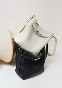 Detailed view of minimalist leather bucket bags in white and black with elegant metallic hardware.