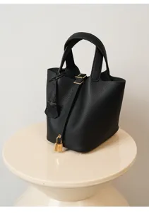 Detalle de bolso cubo de piel negra con textura premium, candado dorado y asa resistente.