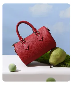 Detailed shot of a red leather Boston bag styled with pears and green moss on table.
