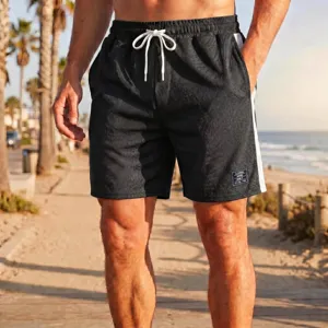Primo piano di pantaloncini sportivi in rete nera con coulisse bianca e bande laterali in spiaggia.