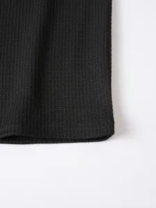 Close-up detail of black waffle knit fabric, showcasing soft texture and neat hemline.