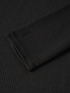 Close-up detail of black waffle knit long sleeve fabric showing rich texture and fine cuff design.