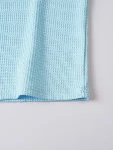 Close-up detail of light blue waffle knit fabric showing premium texture and neat stitching.