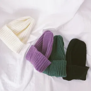 Detail view of soft knit children beanies in four colors white purple green and black.