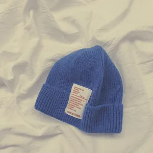 Primo piano dettagliato di un berretto in maglia blu con patch di testo bianco.
