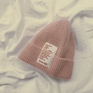 Primo piano di berretto in maglia rosa con patch di testo bianco, cappello casual caldo