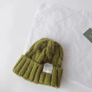 Green cable knit kids beanie with fabric label, warm winter pullover hat for boys and girls.