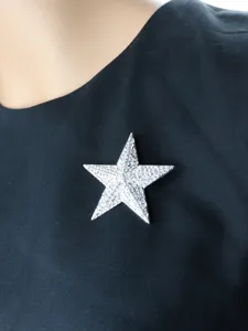 Close-up detail of a sparkling rhinestone pentagram brooch pinned on black fabric.