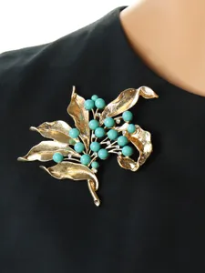 Vintage gold-tone leaf and turquoise bead brooch detail, elegant retro clothing accessory.