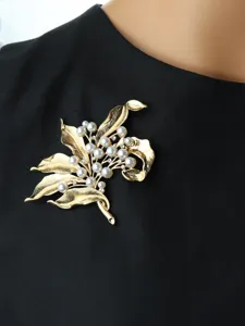 Vintage gold tone floral brooch with faux pearls and rhinestones detail on black apparel.