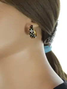 Gros plan de boucles d'oreilles créoles émaillées à damier noir et or, texture détaillée.