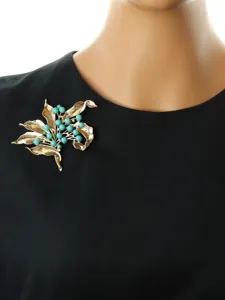 Close-up detail of vintage floral brooch with gold leaves and turquoise beads on black.