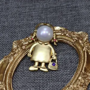 Primo piano dettagliato della spilla vintage bambina in oro opaco con testa di perla e strass scintillanti.
