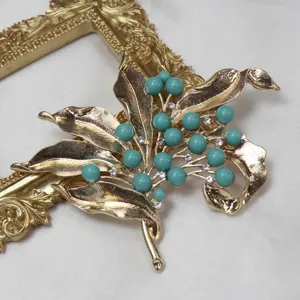 Vintage gold-tone leaf brooch with turquoise beads and clear rhinestones close-up detail shot.