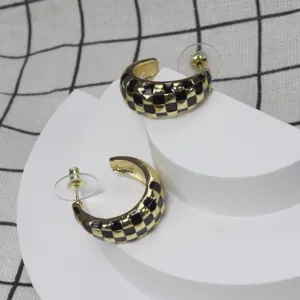 Boucles d'oreilles créoles émaillées à carreaux noir et doré, design géométrique chic.