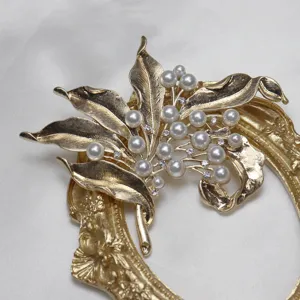 Close-up detail of vintage gold-tone leaf brooch with faux pearls and sparkling rhinestones.