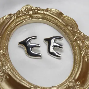 Detailed shot of silver swallow stud earrings set inside vintage gold frame on satin.