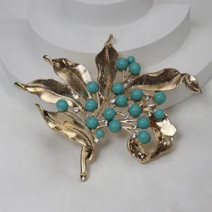 Detailed view of vintage gold-tone leaf brooch with turquoise beads and sparkling rhinestones.