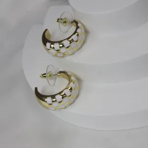 Gros plan des boucles d'oreilles créoles en émail à damier or et blanc montrant la texture.