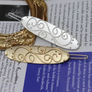 Detail shot of retro embossed metal hair clip featuring intricate scrollwork in gold and silver finish.