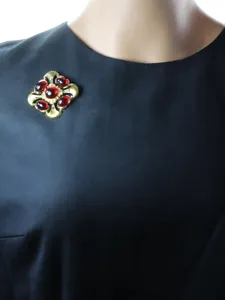 Gros plan d'une broche vintage dorée ornée de cristaux rouges et d'un design délicat.