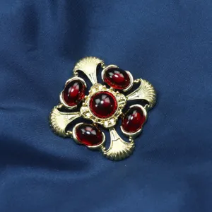 Détail pendentif croix baroque vintage, métal doré ouvragé avec pierres rouges profondes.