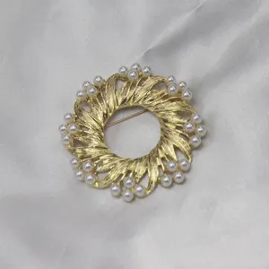 Detaillierte Nahaufnahme einer goldenen Vintage Kranz Brosche mit weißen Perlen.