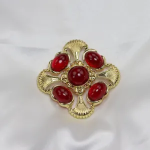 Gros plan détail de la broche pendentif croix creuse dorée vintage avec des pierres rouges.