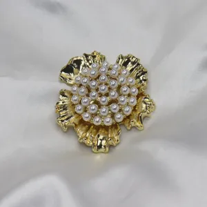 Gros plan détaillé d'une broche florale dorée de style vintage ornée de perles blanches.