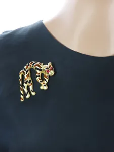 Dettaglio della spilla leopardo vintage con macchie in smalto e pietre rosse sul tessuto.