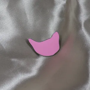Vue de détail d'une broche chat en émail rose, contour métallique, accessoire design minimaliste.