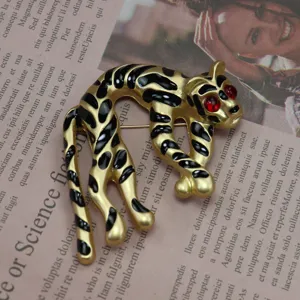 Primo piano di una spilla vintage a forma di leopardo smaltato oro con occhi di gemma rossa.
