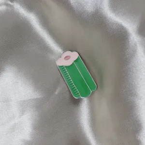 Close-up detail of creative green enamel brooch pin with lovely pink accent on satin fabric.