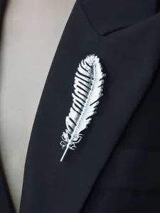 Close-up detail of a silver feather brooch pinned on a black suit lapel, elegant accessory.