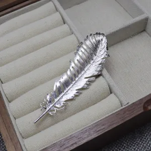 Close-up view of a delicate silver feather brooch displayed inside a luxury jewelry box slot.