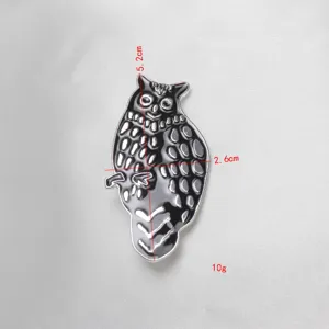 Vista dettagliata di una spilla in metallo smaltato a forma di gufo, dimensioni 5,2x2,6 cm.