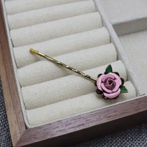 Close-up of a vintage handmade enamel pink rose hair clip detail in a jewelry tray.