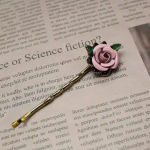 Close-up of vintage pink enamel rose hair clip featuring delicate gold branch and green leaves.