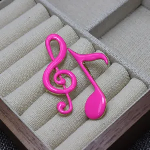 Close-up detail shot of pink enamel music note brooch displayed in beige fabric tray.