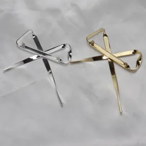 Dettaglio spilla a nastro metallico in oro e argento posata su tessuto satinato.