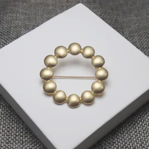 Gold-toned metallic pebble circle brooch, elegant tambourine motif scarf buckle, chic accessory.
